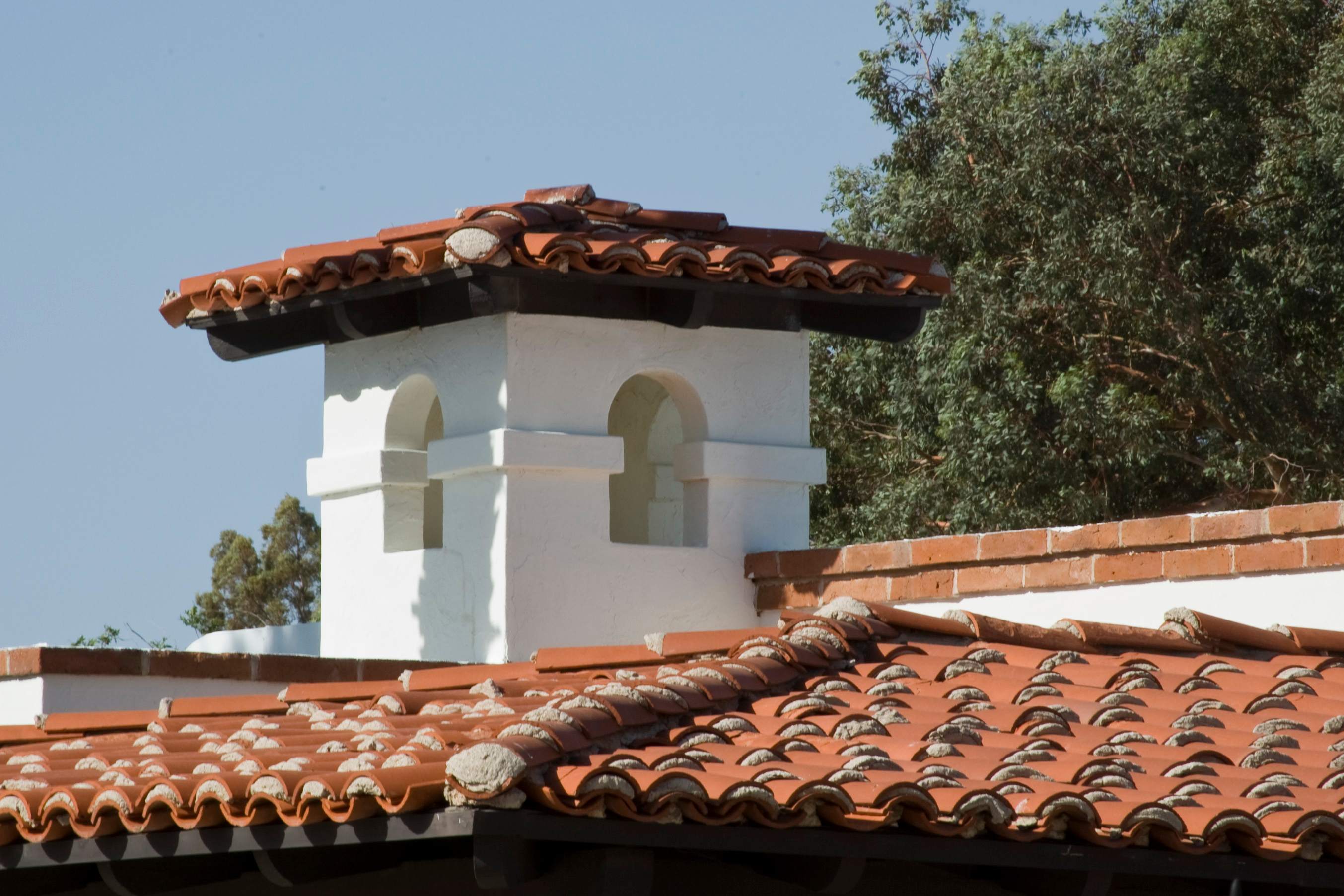 Terracotta tile roof and white stucco walls of a Southwest-style home under a clear sky.