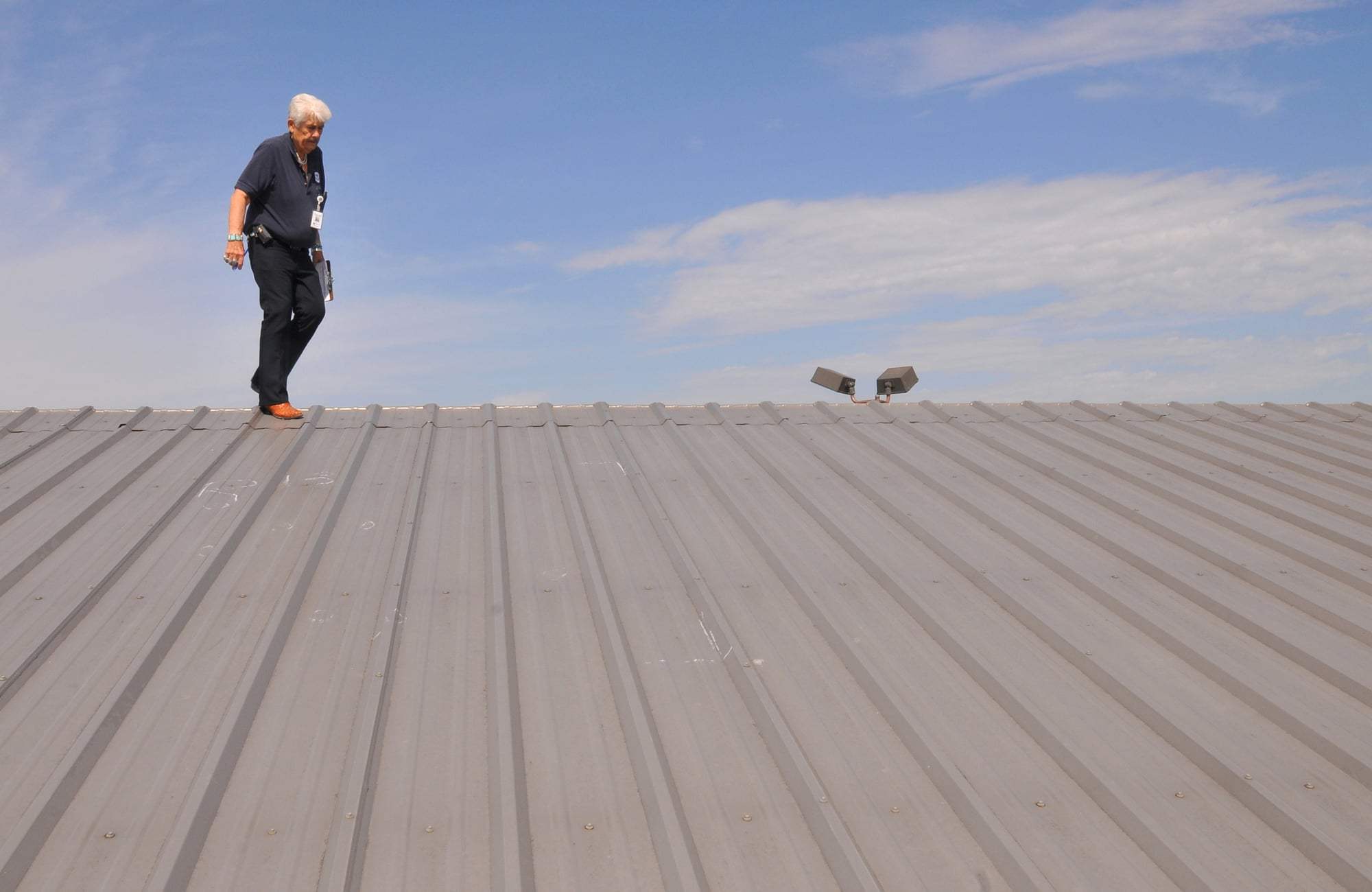 An inspector walking a metal roof, checking the panels for hail damage.